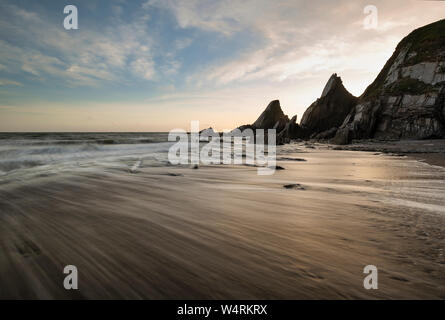 Schönen Sonnenuntergang Landschaft Bild von Westcombe Strand in Devon, England mit gezackten Felsen am Strand und atemberaubende Wolkenformationen Stockfoto