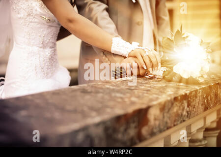 Eine neu Hochzeit paar Legen Sie Ihre Hände auf einer Hochzeit Bouquet zeigen Ihre Trauringe. Stockfoto