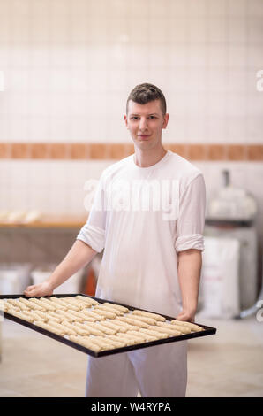 Halbzeuge aus Teig eine junge Bäcker holding Rohstoff der weißen Teig bereit zum Backen im Ofen Stockfoto