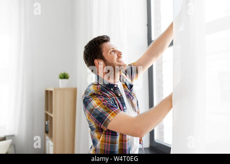 Junger Mann öffnen Fenster Vorhang zu Hause Stockfoto