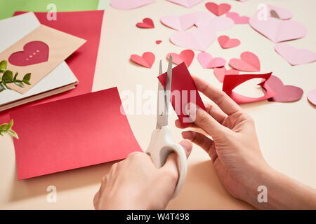 Frau schneidet aus rotem Filz Herzen, hausgemachte Handwerk für Valentinstag, Hand Kreativität, Ansicht von oben Stockfoto