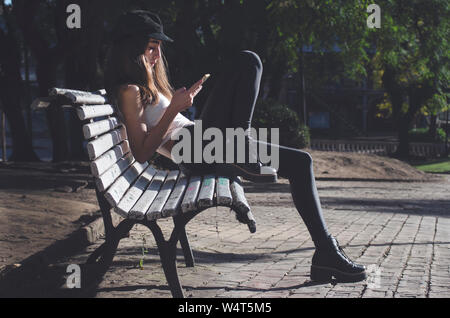 Junges Mädchen sitzen auf einer Bank an Ihrem Mobiltelefon suchen, Argentinien Stockfoto