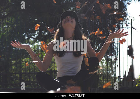 Junges Mädchen sitzt auf dem Boden werfen Blätter in der Luft, Argentinien Stockfoto