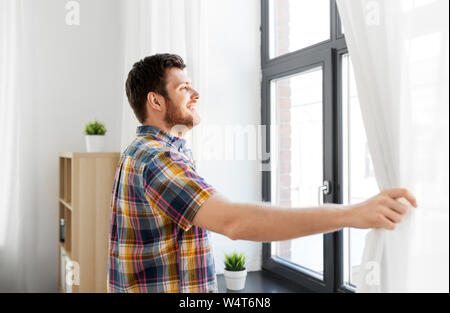 Junger Mann öffnen Fenster Vorhang zu Hause Stockfoto