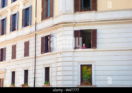 Rom, Italien, 28. Oktober 2017: Eine alte Dame suchen aus einem Fenster mit braunen Fensterläden. Konzept des Lebens, Erinnerungen, Freude. - Bild Stockfoto