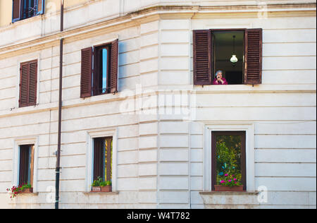 Rom, Italien, 28. Oktober 2017: Eine alte Dame suchen aus einem Fenster mit braunen Fensterläden. Konzept des Lebens, Erinnerungen, Freude. - Bild Stockfoto