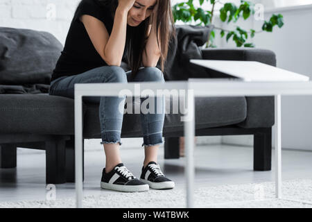 Deprimiert Frau weinen, während auf der Couch zu Hause zu sitzen und die Hände auf den Kopf Stockfoto