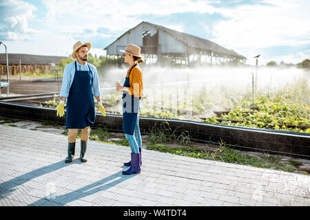 Zwei junge schön gekleidet Landwirte sprechen über das Ackerland mit automatische Bewässerung bei Sonnenuntergang Stockfoto