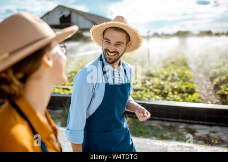 Zwei Jungen, fröhlichen Bauern gehen auf das Ackerland für Schnecken wachsen mit automatische Bewässerung bei Sonnenuntergang Stockfoto