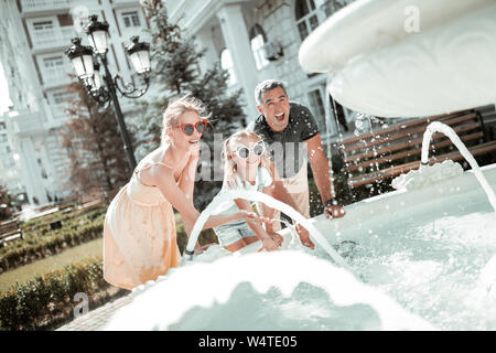 Sommer Spaß. Mutter, Vater und Tochter lachend und sich die Hände waschen in einem Brunnen vor dem Haus. Stockfoto