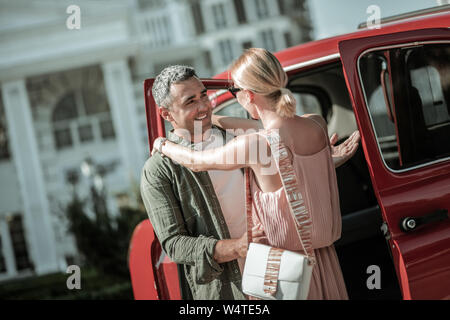 Auf Wiedersehen sagen. Lächelnd Mann nahe sein Auto stehen und seiner schönen Frau umarmen vor Verlassen. Stockfoto