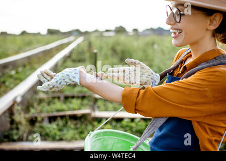 Porträt einer jungen Frau Bauer mit Schnecke auf die Hand, stehend auf dem Ackerland für den Anbau von Schnecken im Freien Stockfoto