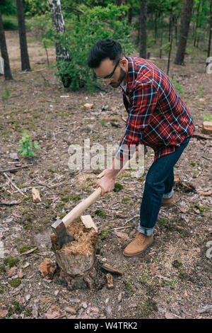 Holzfäller in Plaid Shirt und Jeans Schneiden von Holz mit Axt im Wald Stockfoto