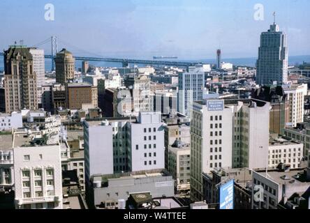 Luftaufnahme der Städtischen Skyline von Downtown San Francisco, Kalifornien, USA, auf der Suche nach Osten in Richtung der San Francisco Bay, mit Welcome Wagon Gebäude, Hotel Drake Wiltshire, die Bank von Amerika Gebäude, 76 Benzin Zeichen, West Coast Leben Gebäude, Cook's Travel Service Reklametafeln und die Oakland San Francisco Bay Bridge sichtbar, mit einem Schiff in den Hafen von San Francisco in der Ferne, an einem sonnigen Tag, Farbe Bild auf Kodachrome film, 1962. () Stockfoto