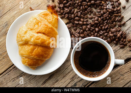 Kontinentales Frühstück mit frischen Croissants und heißen Kaffee auf hölzernen Hintergrund, Deko mit Kaffeebohnen Stockfoto