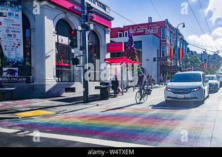 Radfahrer und Autos sind sichtbar, nähert sich der Regenbogen Crosswalk, Teil des Regenbogens Ehre Spaziergang zum Gedenken an LGBT-Führer, auf der Castro Street in der Castro District von San Francisco, Kalifornien, USA, als eines der wichtigsten Zentren der LGBT-Kultur in den Vereinigten Staaten bekannt, Dezember, 2018. () Stockfoto