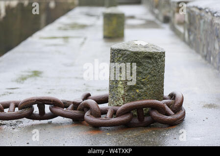 Großen rostigen Angeln boot Kette eingeschleift um eine konkrete Liegeplatz auf einem nassen Hafen (Hafen) Wand. Stockfoto