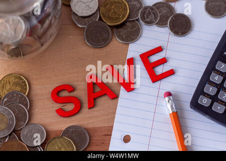 'Speichern' in Holz- buchstabensteine mit Geld, Bleistift, Papier und Taschenrechner geschrieben, um das Wort. Stockfoto