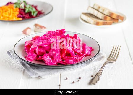 Konserven fermentiert lila Kraut mit Rüben, Karotten und Knoblauch auf einer weißen Platte, auf einer weißen Serviette, auf einem hellen, natürlichen Tabelle, in einer horizontalen orientatio Stockfoto