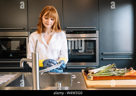 Weiße Frau mit Handschuhen gereinigt Gerichte in der Küche Stockfoto