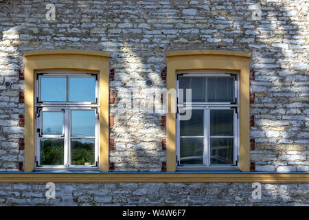 Zwei rechteckigen Fenstern mit gelben Holzrahmen auf dem Hintergrund einer Mauer aus Stein mit einem Schatten aus dem Baum. Vom Fenster aus der Serie der Welt. Stockfoto