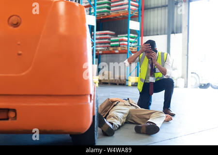 Männliche supervisor Gespräch am Handy, während seine Kollegen bewusstlos auf dem Boden Stockfoto