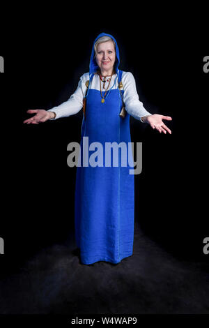 Eine reife Frau in einem T-Shirt und ein blaues Kleid aus einem Viking-Ära hangerok streckt die Hände in einer einladenden Geste gekleidet. Stockfoto