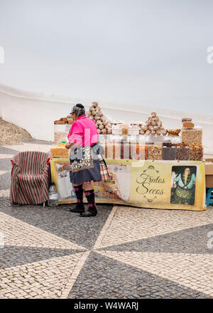 Nazare, Portugal - 19 Juli 2019: Eine lokale Frau in traditioneller Kleidung verkauft Obst am Miradouro getrocknet Stockfoto