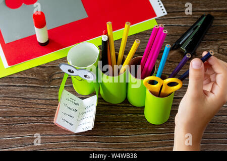 Das Kind bringt die Bleistifte in Papierrolle Bleistifthalter das neue Schuljahr auf hölzernen Tisch. Zurück in der Schule willkommen. Kinder- Kunstprojekt, Handarbeit Stockfoto