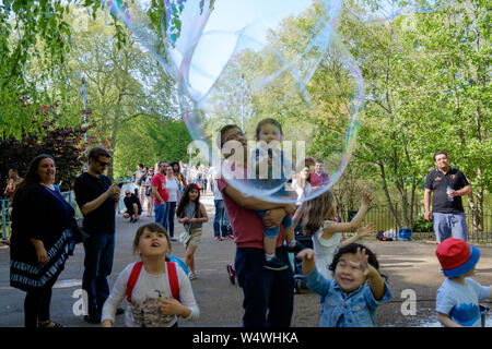 Kinder spielen mit großen Seifenblasen in St James's Park, Central London, UK an einem warmen Tag. Stockfoto