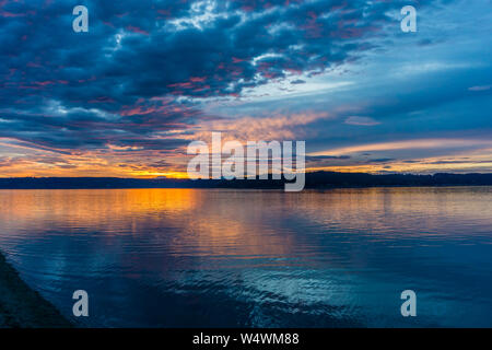 Die Wolken hängen am Himmel, wie die Sonne hinter den Olympic Mountains im Armaturenbrett, Washington. Stockfoto