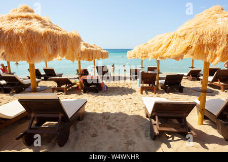 Strand schöne strohgedeckten Sonnenschirmen und leuchtend türkisfarbene Meer, tolle Erholung und Entspannung. Stockfoto