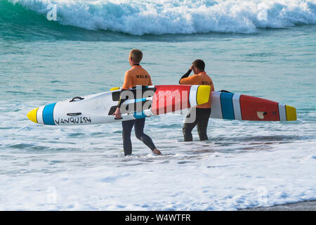 Mitglieder von Newquay Surf Life Saving Club Durchführung Vanquish Lebensrettende Race Boards starten eine Schulung bei Fistral in Newquay in Cornwall. Stockfoto