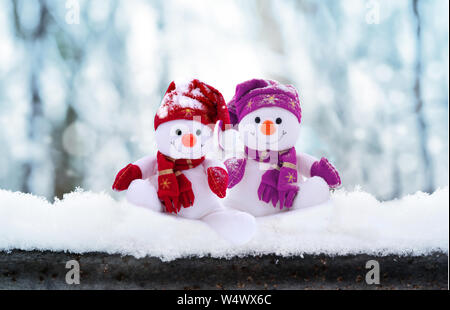 Zwei kleine Schneemänner das Mädchen und der Junge in Mützen und Schals auf Schnee im Winter. Festliche Hintergrund mit einem lustigen Schneemann. Weihnachtskarte, kopieren. Stockfoto