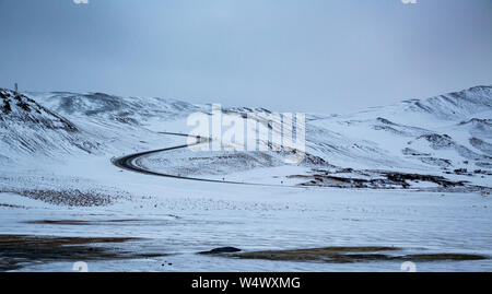 Horizontale Aufnahme einer S-förmigen Straße, die in Island von Schnee umgeben ist Stockfoto
