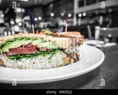 Nahaufnahme eines Toastsandwiches mit Avocado-Scheiben und Salami Auf einem runden weißen Teller Stockfoto