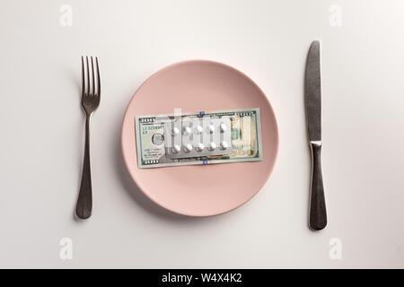 Pillen und Geld auf den Teller mit Messer und Gabel auf weißem Hintergrund Stockfoto