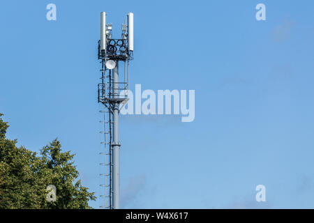 Graue Leitung Telekommunikationsturm mit der Oberseite der Grüne Baum auf blauen Himmel mit Wolken Hintergrund, Stockfoto