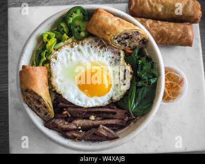 Ein Schuss von einem Gericht mit Spiegeleiern und Fleisch Mit Gemüse und Frühlingsrollen darauf Stockfoto