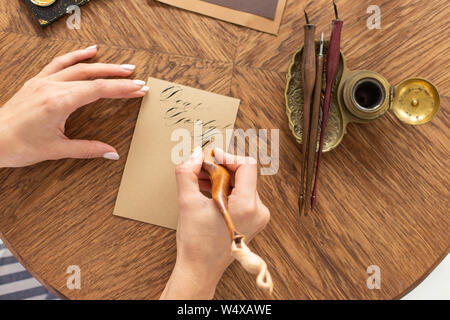 Kalligraph hält einen Stift mit Tinte. Das Mädchen schreibt einen Brief in handschriftlichen Font. Kreative Werkstatt des Künstlers. Soft Focus. Stockfoto