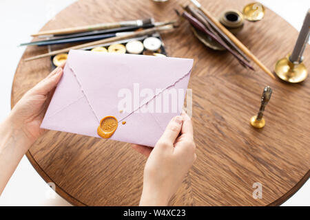 Weibliche Hände halten einen Umschlag mit einem Buchstaben und einer surgut Dichtung. Geschenkgutschein. Hochzeit Einladung. Soft Focus Stockfoto