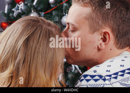 Verliebtes Paar sitzt neben einem Weihnachtsbaum, tragen warme Pullover, umarmen und weg von der Kamera auf den Baum. Stockfoto