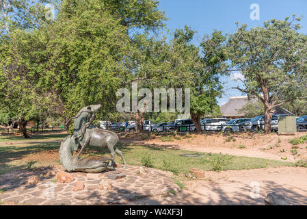 Krüger National Park, Südafrika - 5. Mai 2019: Eine Szene in der SKUKUZA Restcamp. Personen, Fahrzeugen und einer Statue von zwei Kudu Bullen kämpfen visibl Stockfoto