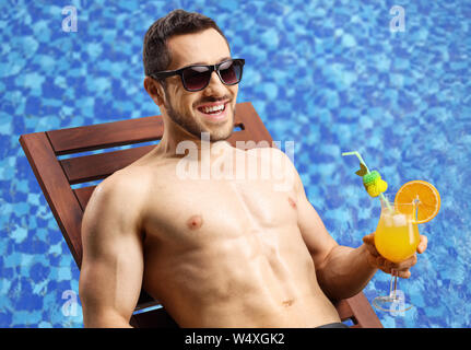 Hübscher junger Mann auf einer Liege mit einem Cocktail am Pool Stockfoto