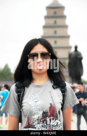 Ein verspielter chinesische Frau ihre Zunge heraus in der Nähe von Buddha Statue in der Nähe der Großen Wildgans-Pagode in der Stadt Xian in der Provinz Shaanxi in China. Stockfoto