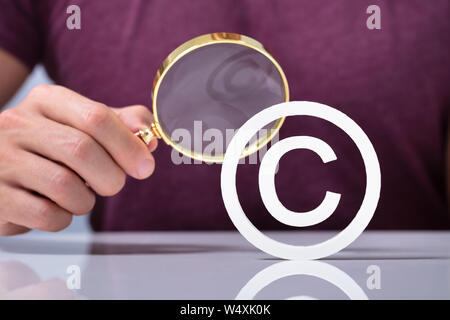 Eine Hand mit Lupe Suchen Copyright Symbol Symbol über Schreibtisch Stockfoto