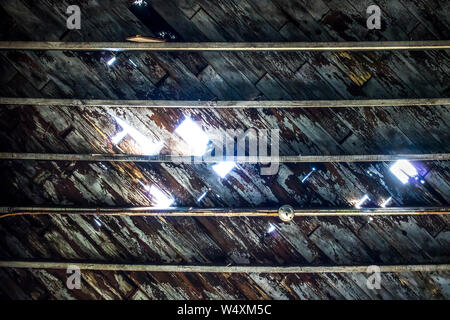 Abblätternde Farbe auf alten Holzdecke von unten. Licht kommt durch, wo Schindeln in verlassenen industriellen cannery Lager ausgehöhlt haben. Stockfoto