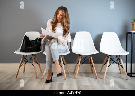 Junge Geschäftsfrau Ordner beim Sitzen auf Stuhl warten auf Job Interview Stockfoto