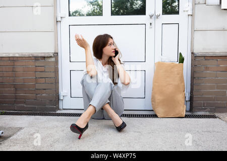 Eine Angst junge Frau sitzt vor der Tür Sprechen auf Mobilephone Stockfoto