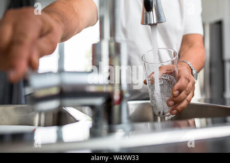 Hände eines älteren Mannes gießen ein Glas Wasser in eine moderne Küche Stockfoto